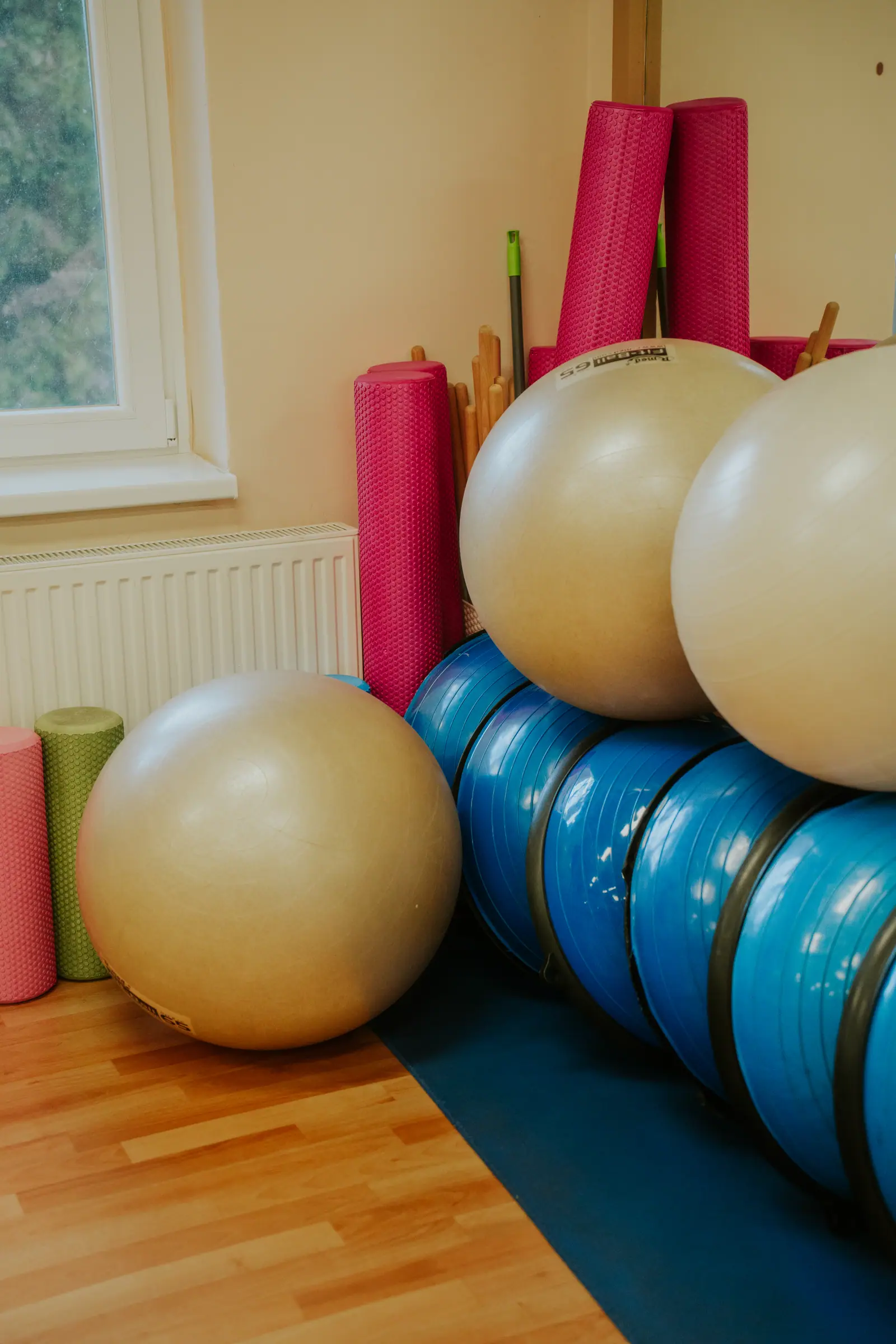 Fitneszlabdák, BOSU labdák és rózsaszín SMR hengerek a terem sarkában az ablak mellett