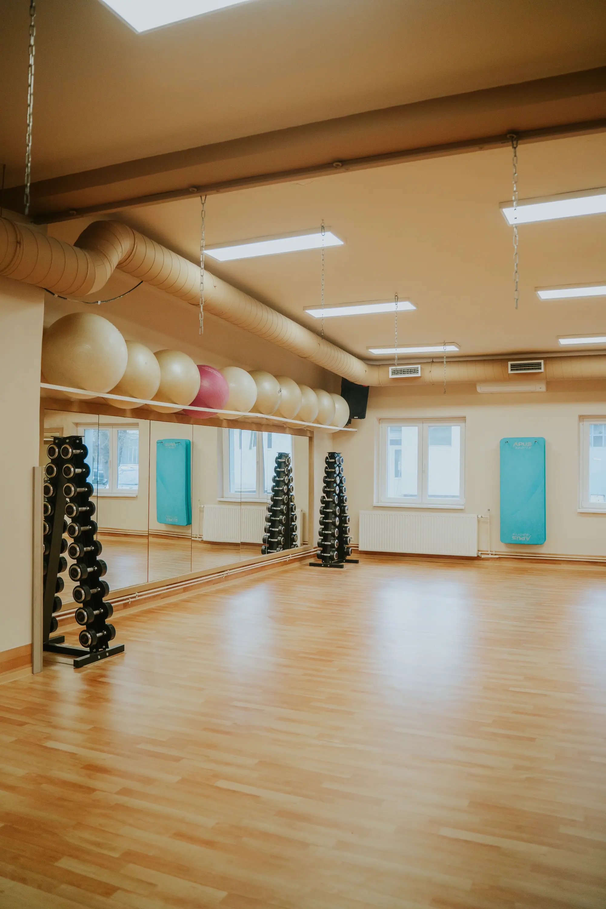 Tágas aerobik terem parkettával, súlyzóállványokkal, fitneszlabdákkal és ablakokkal