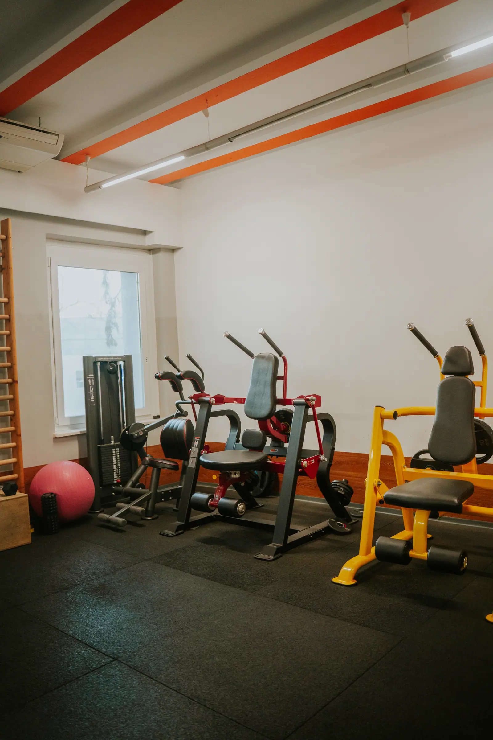 Kisebb edzőterem tárcsás erőgépekkel, kábeles géppel, bordásfallal és fitneszlabdával